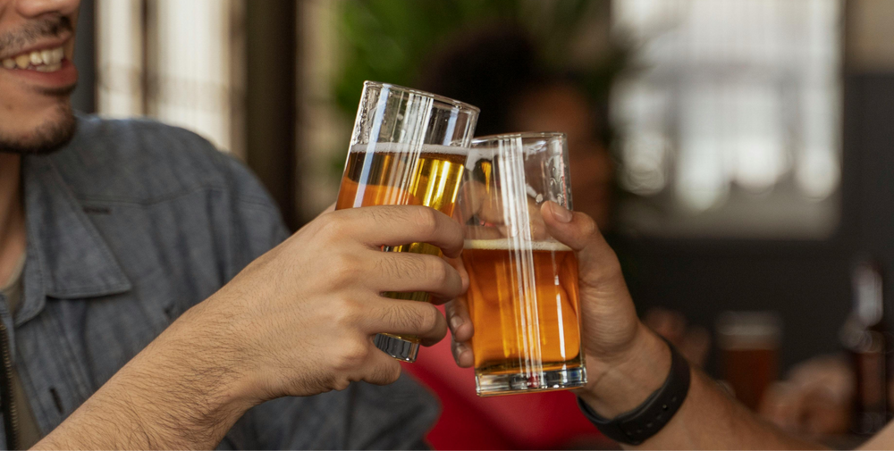 Two people clicking beer glasses, highlighting the connection between alcohol and exercise recovery conversations.