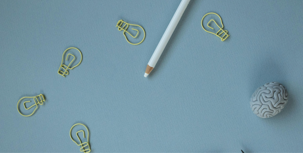 A white pencil, lightbulb-shaped paper clips, and a brain-shaped object representing the concepts of habit formation